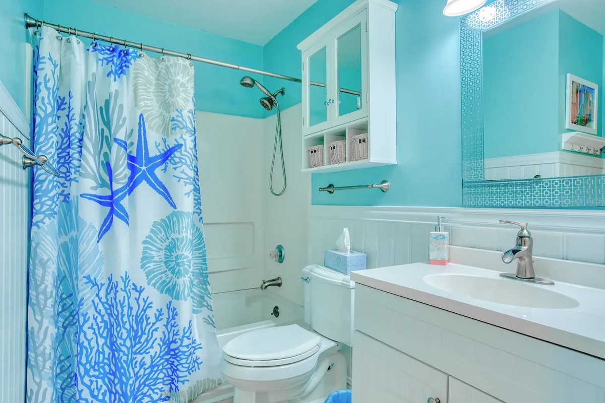 A cheerful bathroom featuring a modern vanity with large mirror, complemented by a colorful shower curtain. The bright and clean space hints at updated fixtures and a welcoming atmosphere for self-care.