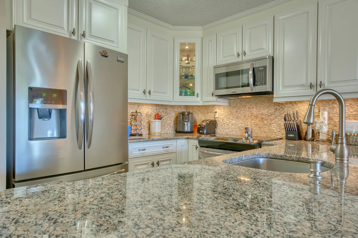 A spacious, modern kitchen with a large granite-topped island, stainless steel refrigerator, ample cabinetry, and various contemporary appliances. The layout is ideal for cooking together or hosting family gatherings.