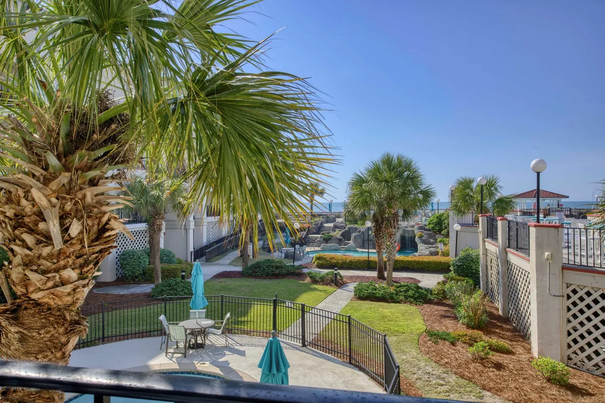 An inviting pool area framed by palm trees, comfortable outdoor seating, and a fenced garden. The scene is softly lit, suggesting a tranquil, leisurely environment perfect for unwinding after a day on the beach.