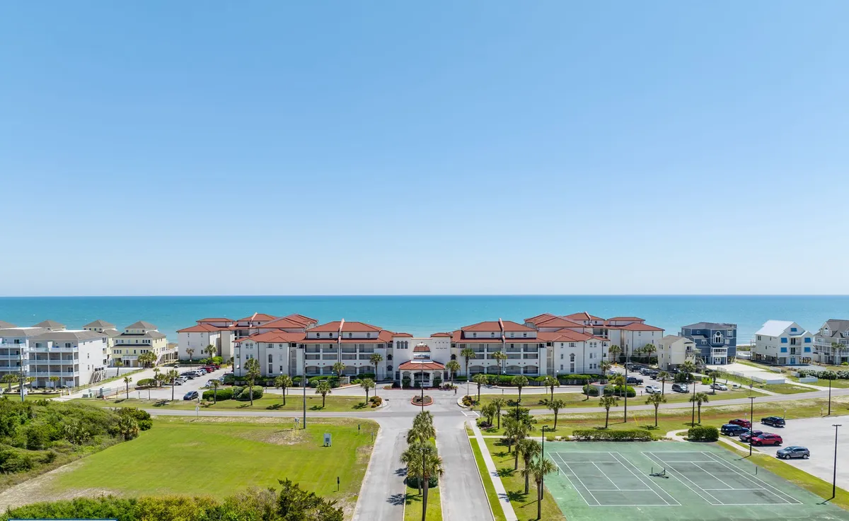 A broad view of a beachfront property showcasing a large swimming pool, adjacent tennis courts, and manicured gardens, all set against the backdrop of the ocean. This scene highlights options for swimming, sunbathing, family gatherings, and active recreation steps from the property.