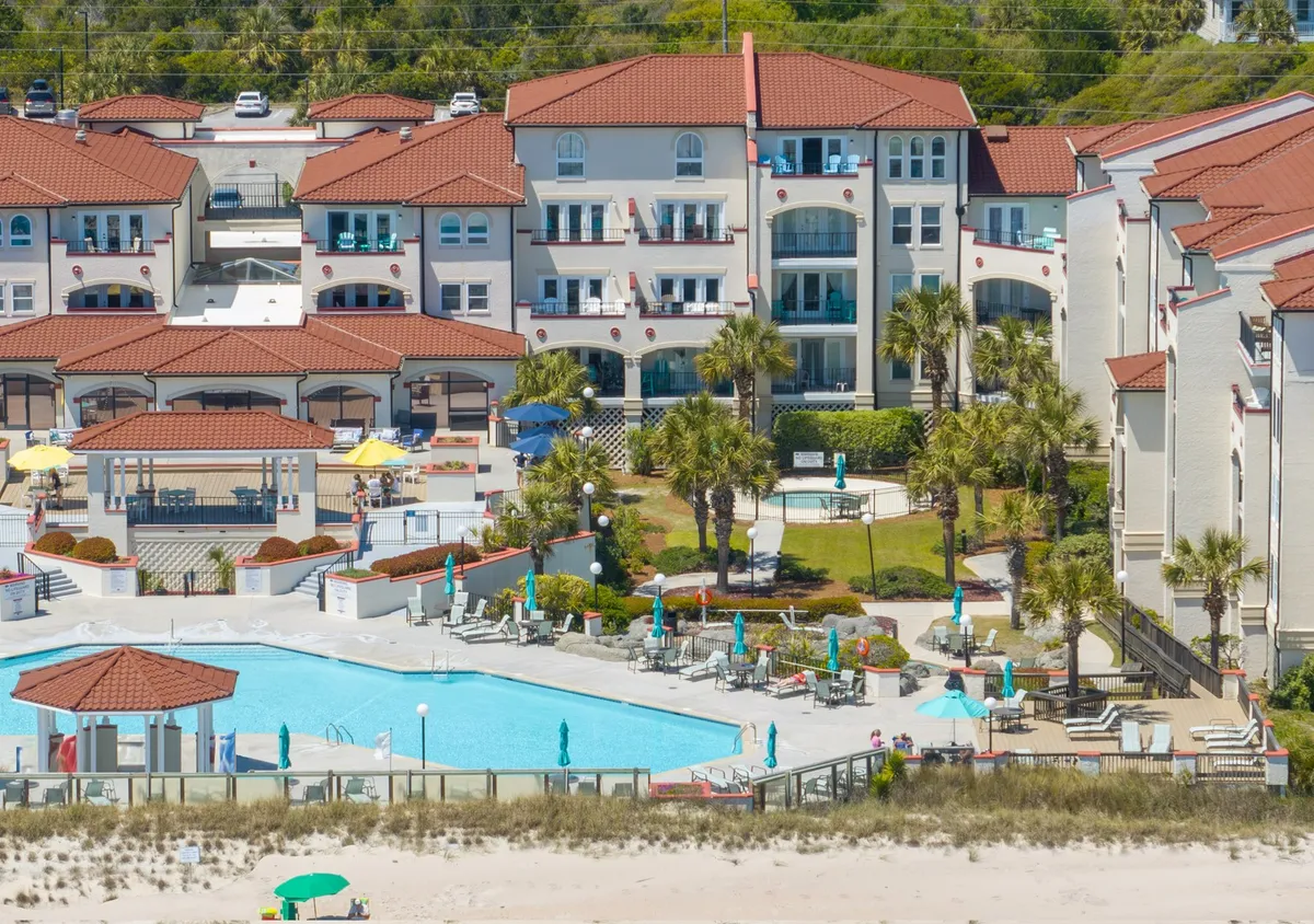 A vibrant, sun-filled pool area with palm trees, comfortable lounge chairs, and visible building architecture. The scene exudes a relaxed, family-friendly atmosphere where children can play and adults can unwind by the poolside.